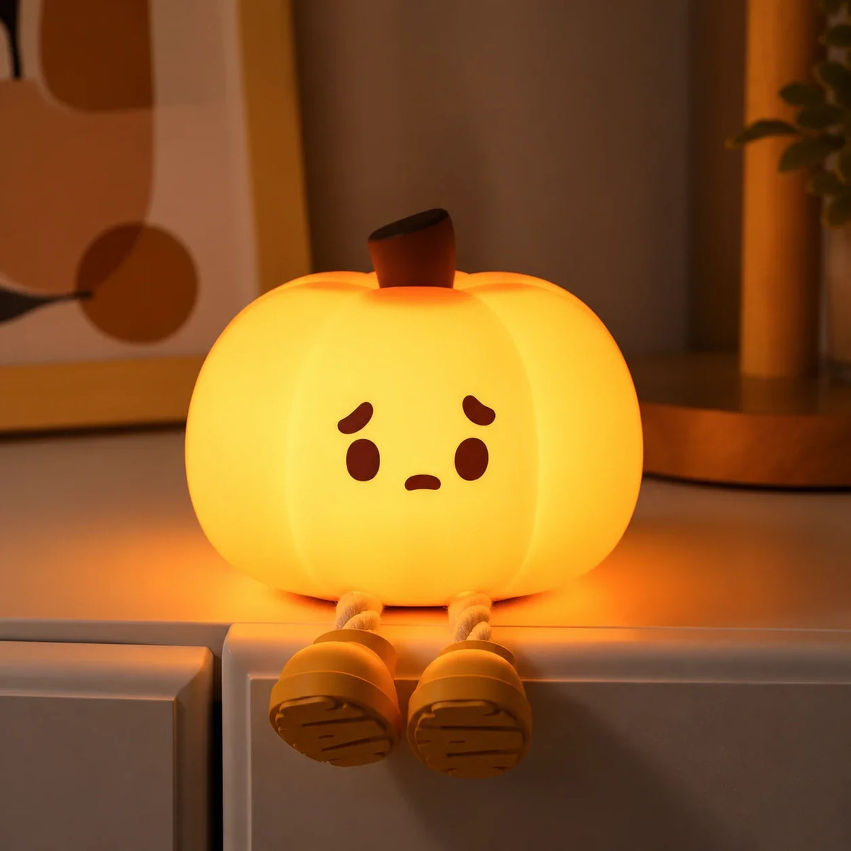 Pumpkin Glow lit up on the edge of a shelf, with its little legs dangling